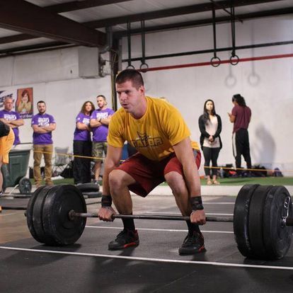 Focused male athlete in a yellow t-shirt performing a heavy deadlift at a Kansas Strength and Performance competition, demonstrating extreme strength.