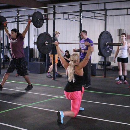 Dynamic group fitness class in action at Kansas Strength and Performance gym, with participants performing barbell exercises.