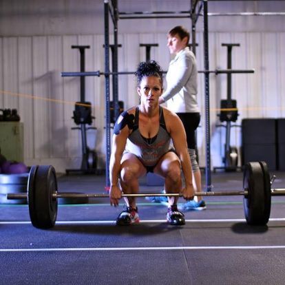 Determined woman setting up to lift a loaded barbell at a strength training session in a gym, exemplifying focus and strength.