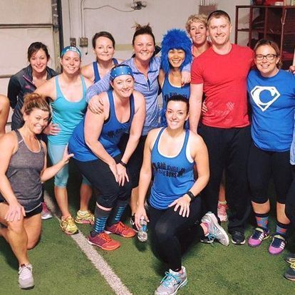 Group of energetic gym members in blue and teal fitness attire smiling together after a workout session at Kansas Strength and Performance gym.