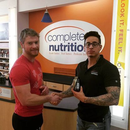 Kansas City Strength and Performance staff member shaking hands with a customer at Complete Nutrition store, celebrating a successful product recommendation.