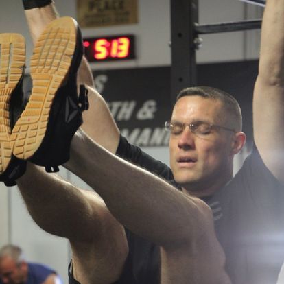 Focused male athlete performing an elevated leg stretch in a gym, under a digital clock displaying workout session time, enhancing flexibility and endurance.