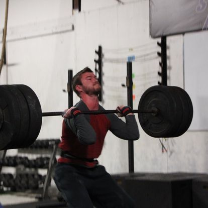 Athlete performing a heavy squat with a barbell at a powerlifting event, showcasing intense concentration and physical strength.