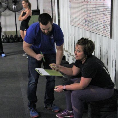 Fitness coach discussing performance and strategies with a female athlete in a gym, using a clipboard for tracking progress.