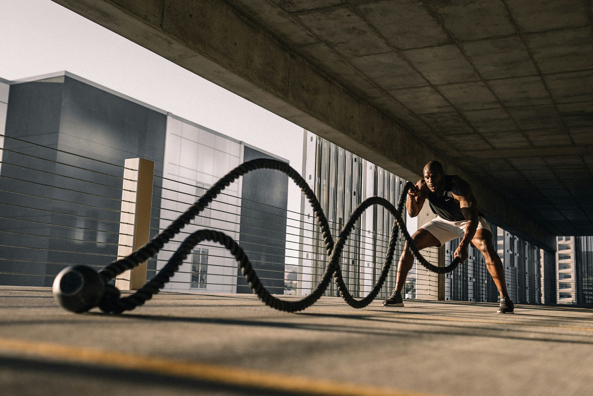 A man in athletic wear using battle ropes for exercise in an urban setting.