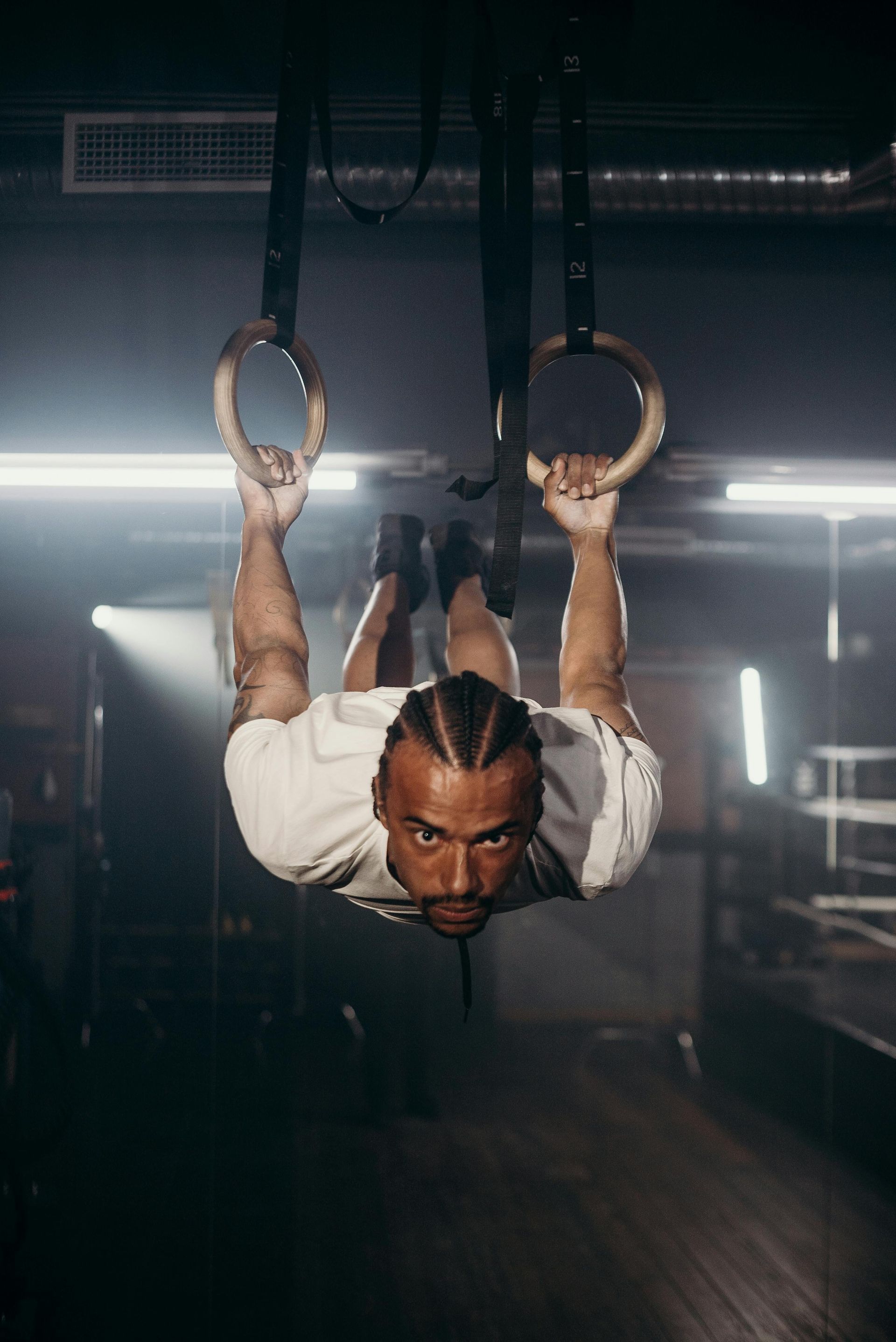 Man doing an exercise on gymnastic rings in a dimly lit gym.