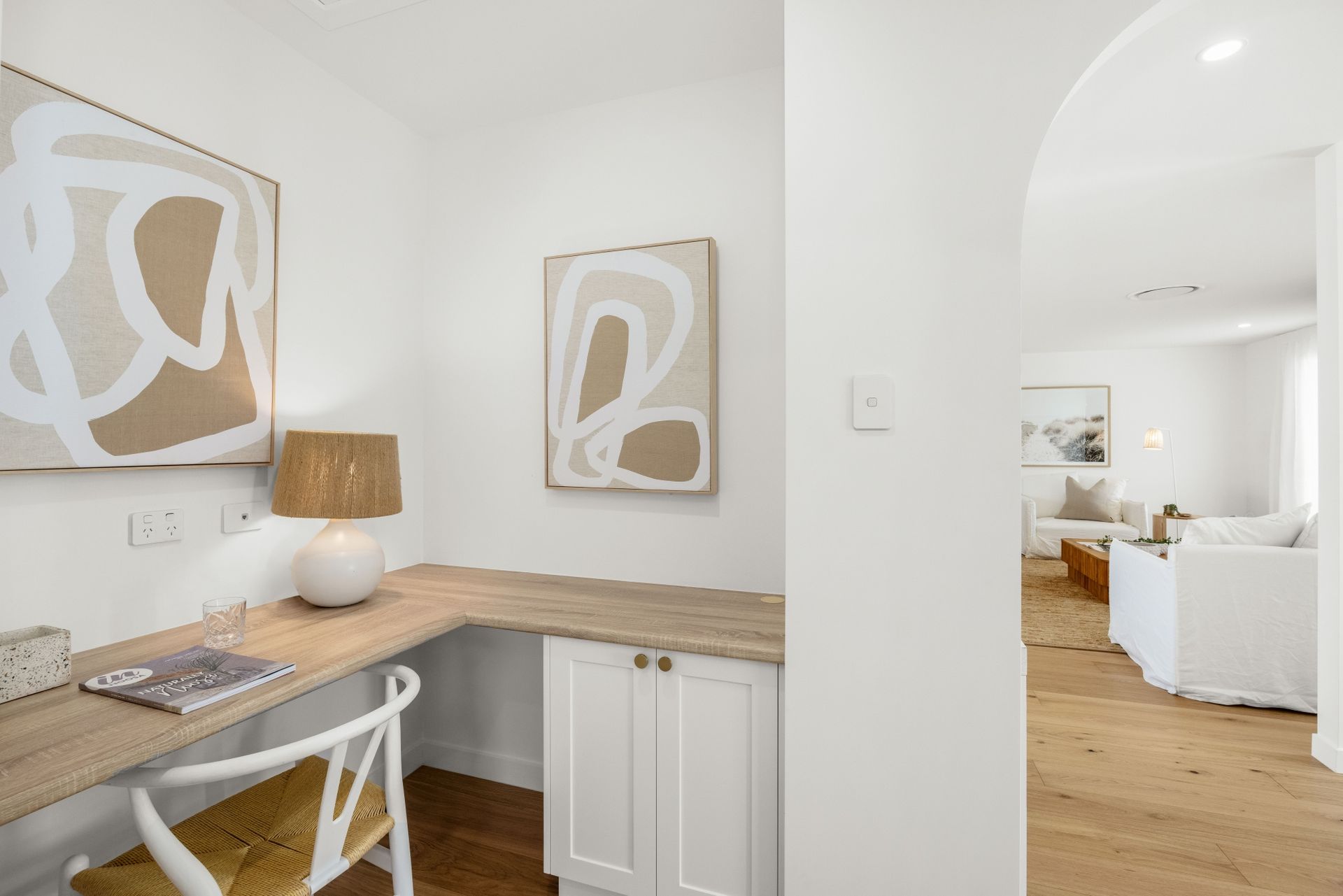 A home office with a desk , chair , lamp and paintings on the wall.