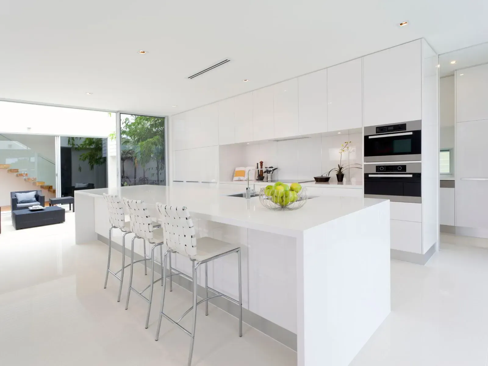 A kitchen with white cabinets and stools and a large island.