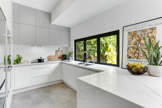 A kitchen with white cabinets , a sink , a refrigerator , and three windows.