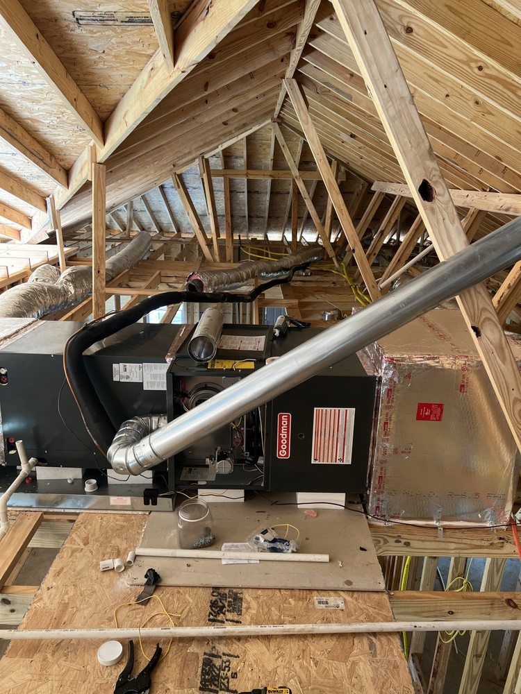 A horizontal furnace unit and ductwork installed in an unfinished attic with wooden roof trusses and insulation.