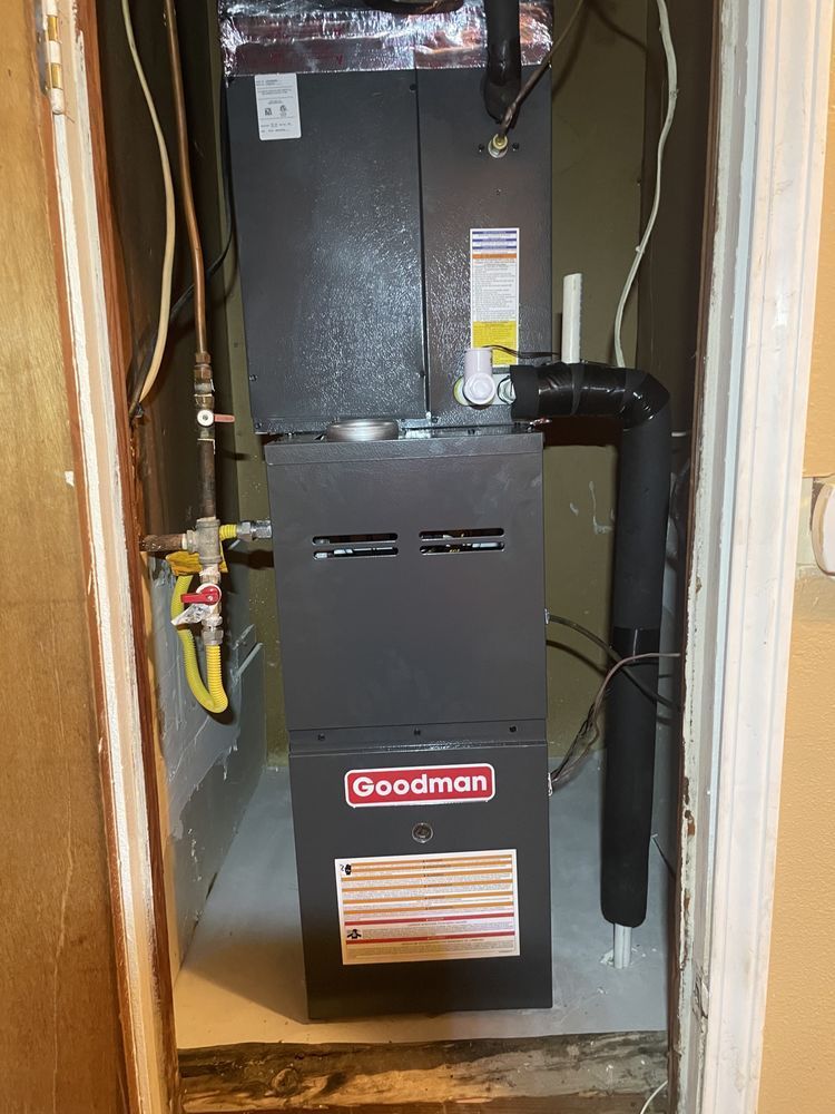 A grey Goodman HVAC unit standing in a small, enclosed utility closet.