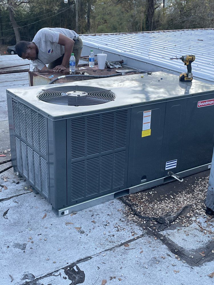 A technician works on a commercial HVAC unit on a flat rooftop, with tools nearby.