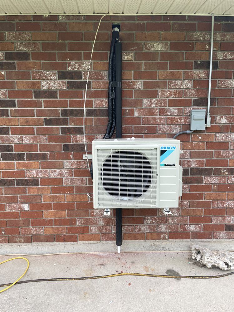 A Daikin HVAC outdoor unit mounted on a brick wall with black piping running vertically up to the roof eaves.