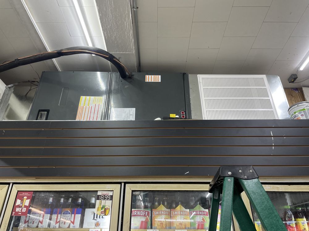 An HVAC unit with a large white intake filter sits on a dark-slatted wall above refrigerated beverage coolers.