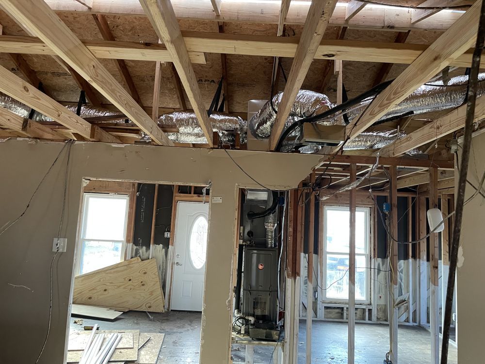 A construction site interior showing exposed wooden ceiling joists, insulated air ducts, and framing for new walls.