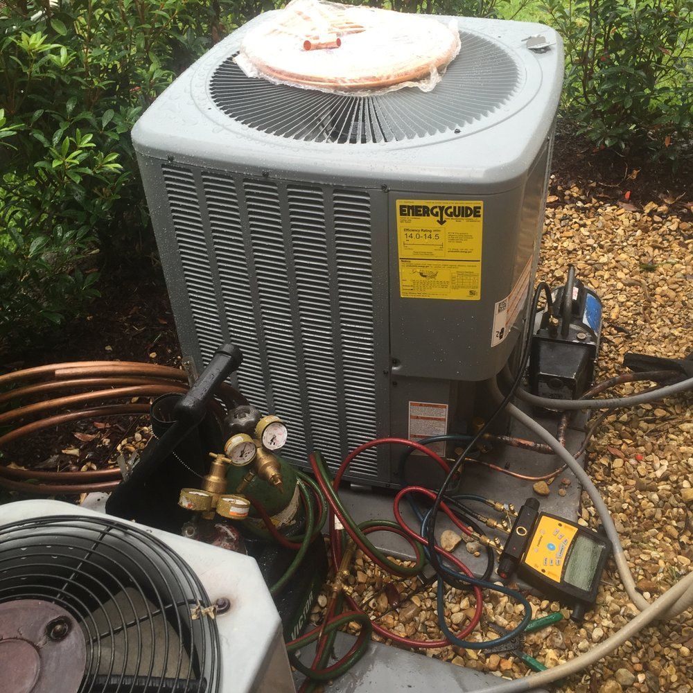 An outdoor air conditioning unit with maintenance tools, gauges, and a vacuum pump set up on gravel for service.