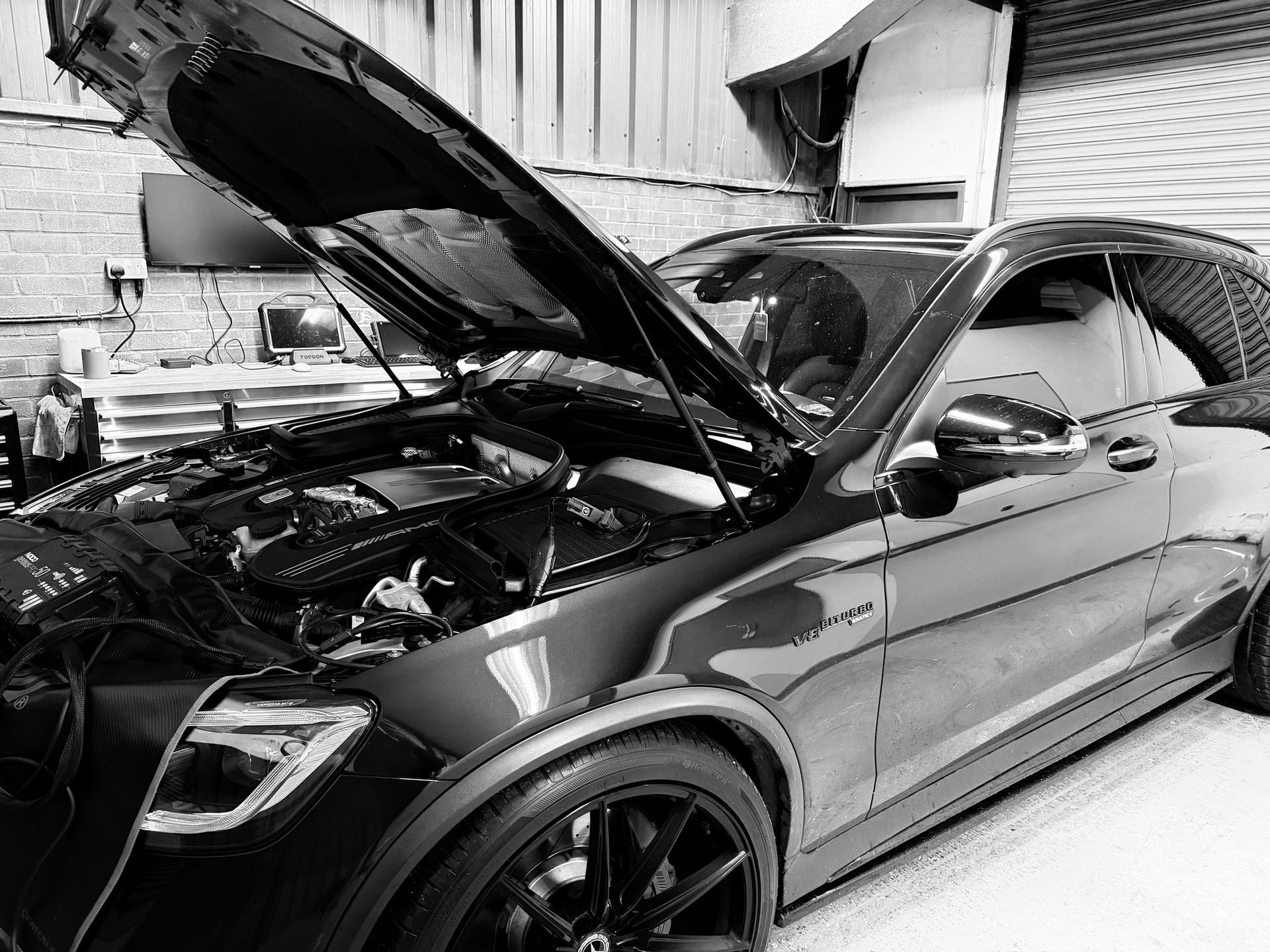 A black Mercedes-AMG with its hood open, parked inside a garage workshop.