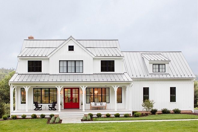 White farmhouse with red front door, covered porch, and metal roof.