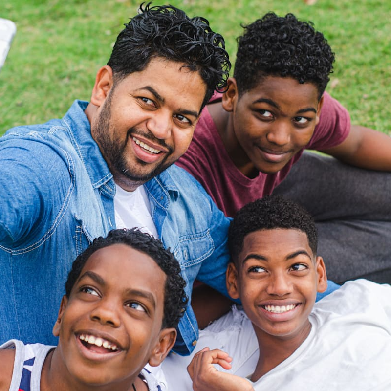 Father and three sons smiling for a selfie outdoors on the grass.