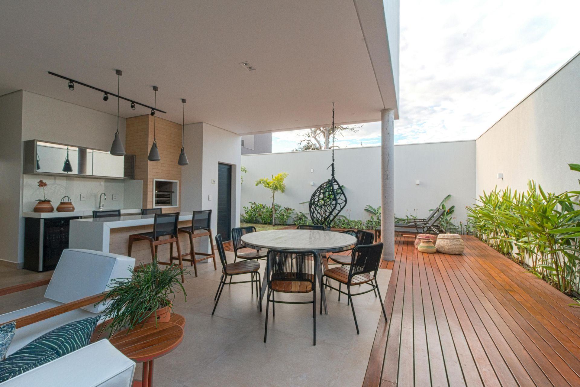 Modern outdoor patio with dining table, kitchen bar, lounge seating, and wooden deck under a covered roof
