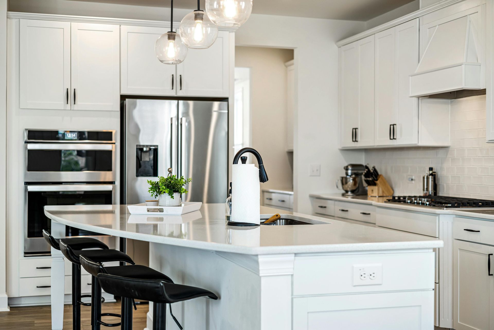 Bright white kitchen with island, barstools, stainless steel appliances, and pendant lights