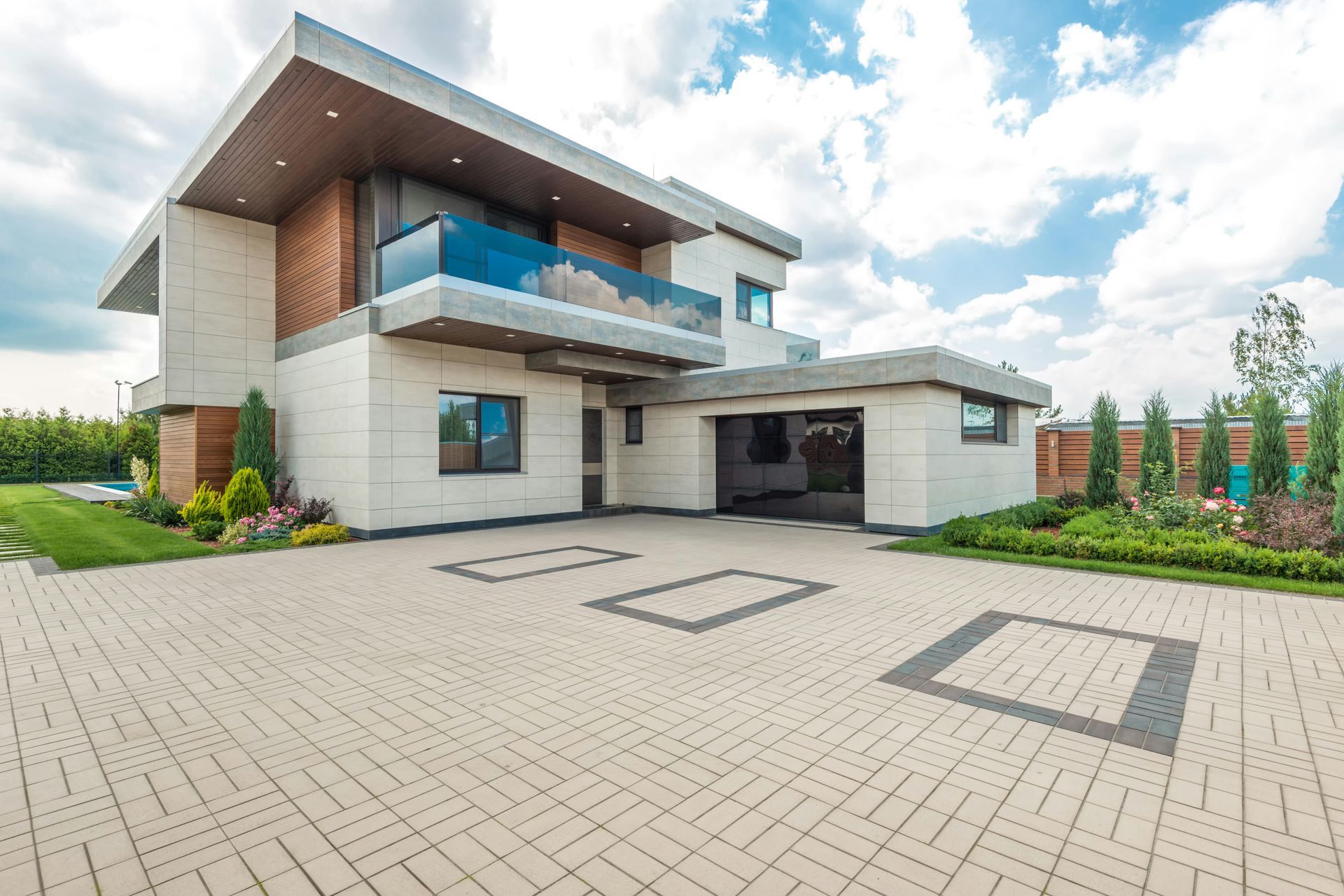 Modern two-story house with brick and white exterior, balcony, and paved driveway under a cloudy sky
