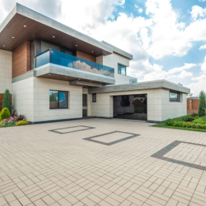 Modern two-story house with a large paved driveway and blue glass balcony under a partly cloudy sky