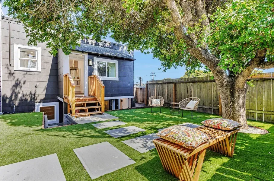 Backyard with small blue shed, wooden steps, lawn, patio stones, chairs, and a large tree