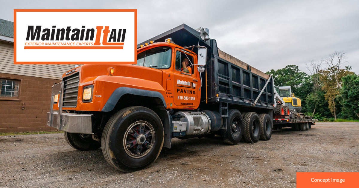 An orange MaintainItAll dump truck pulling a flatbed trailer with a piece of yellow construction equipment on gravel.