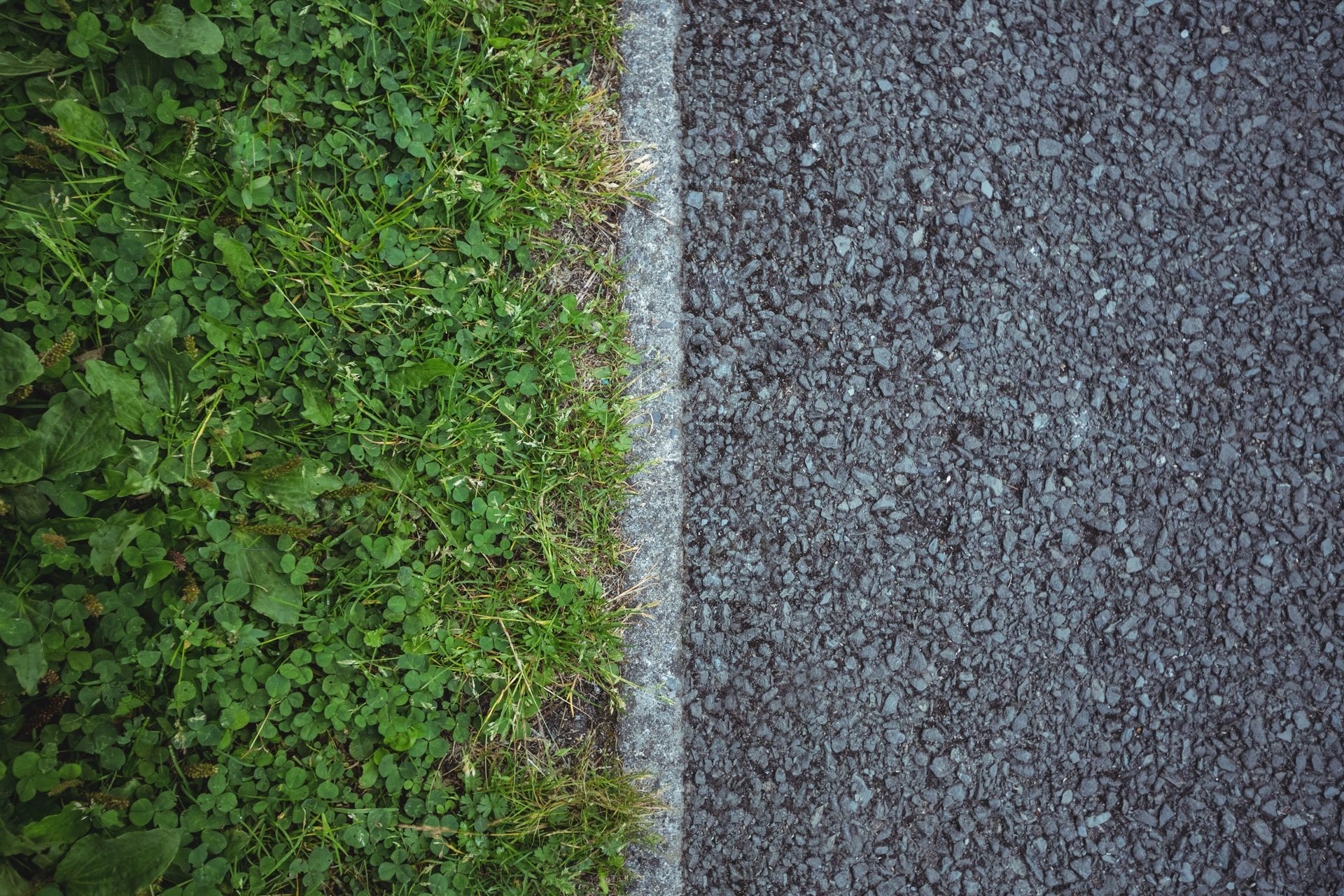A top-down view showing a vertical border line separating green grass on the left from grey asphalt on the right.