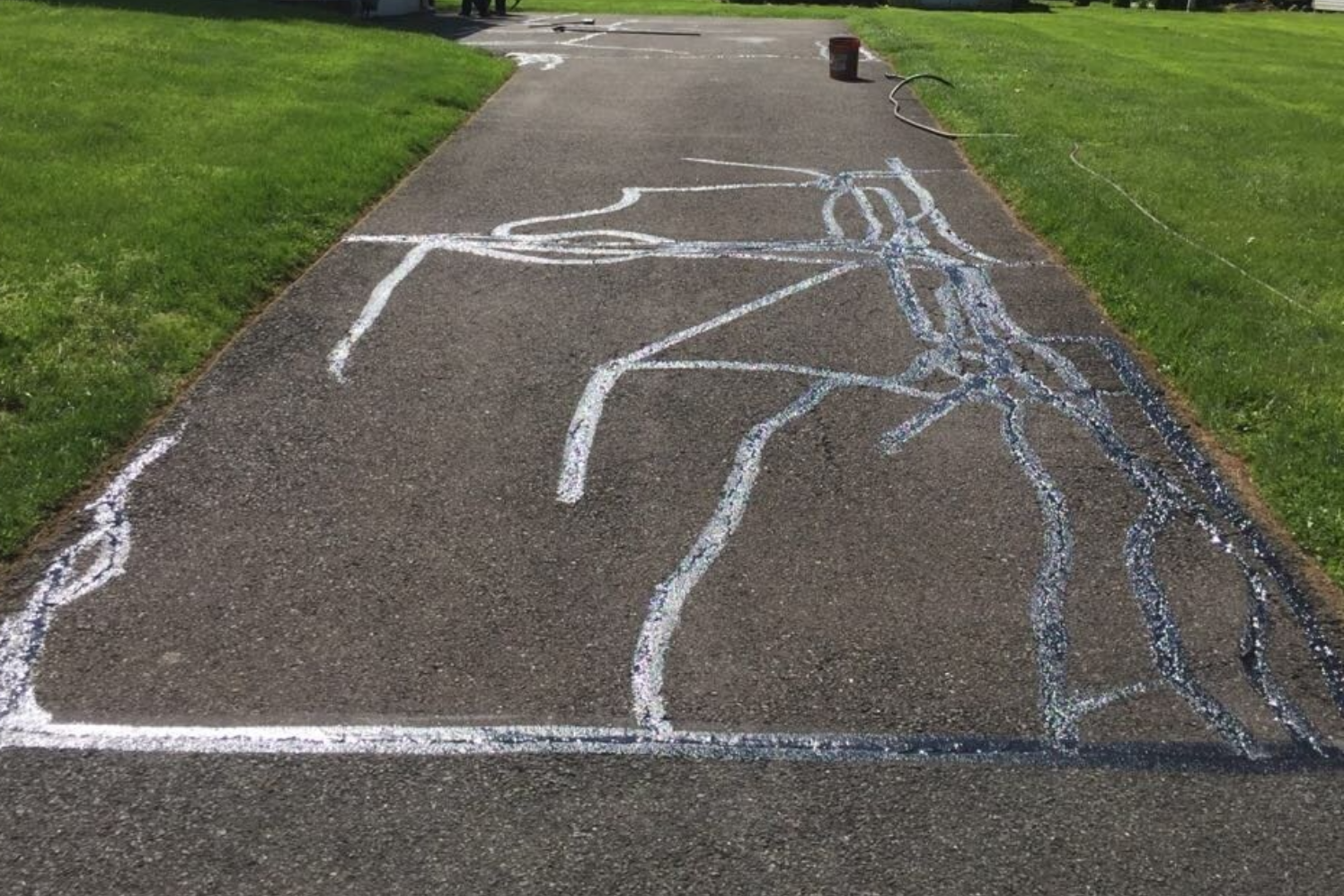Asphalt driveway with white crack sealant. Green grass borders the path.