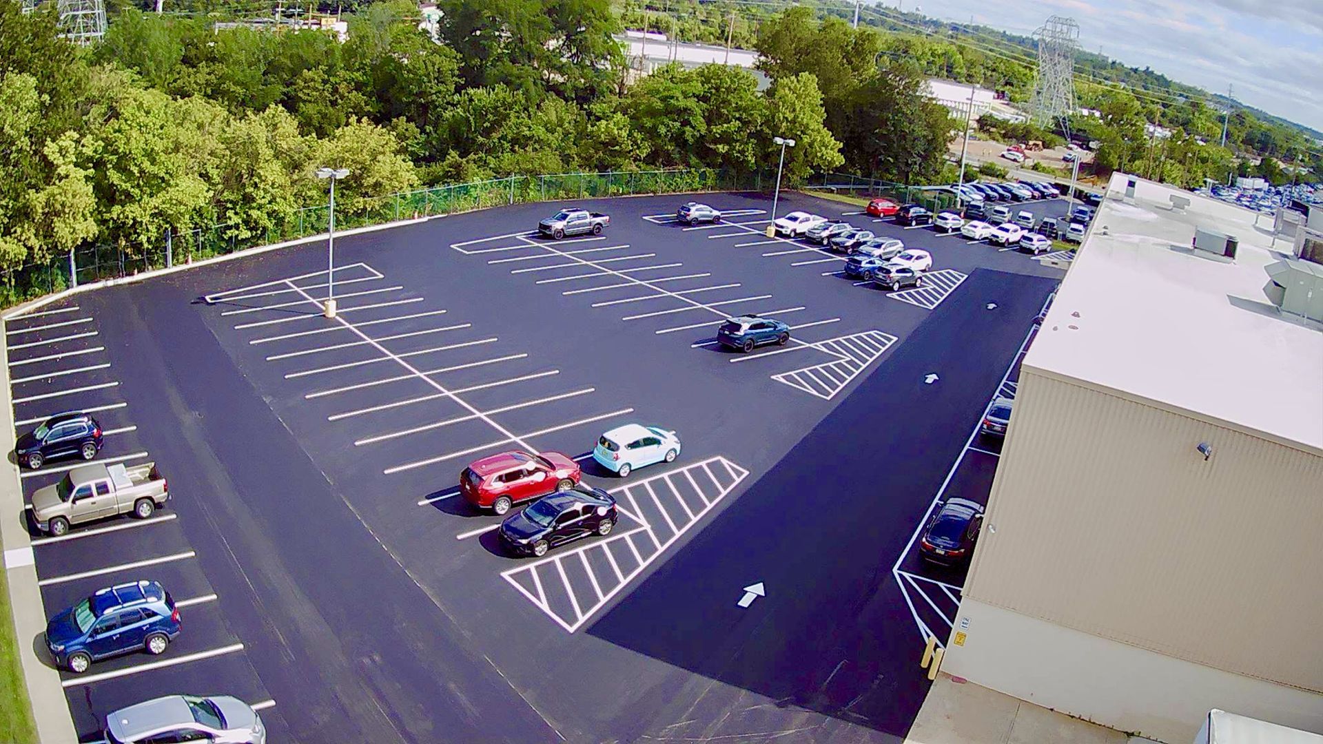 Aerial view of a freshly paved parking lot with marked white stalls and several cars parked in the spaces.