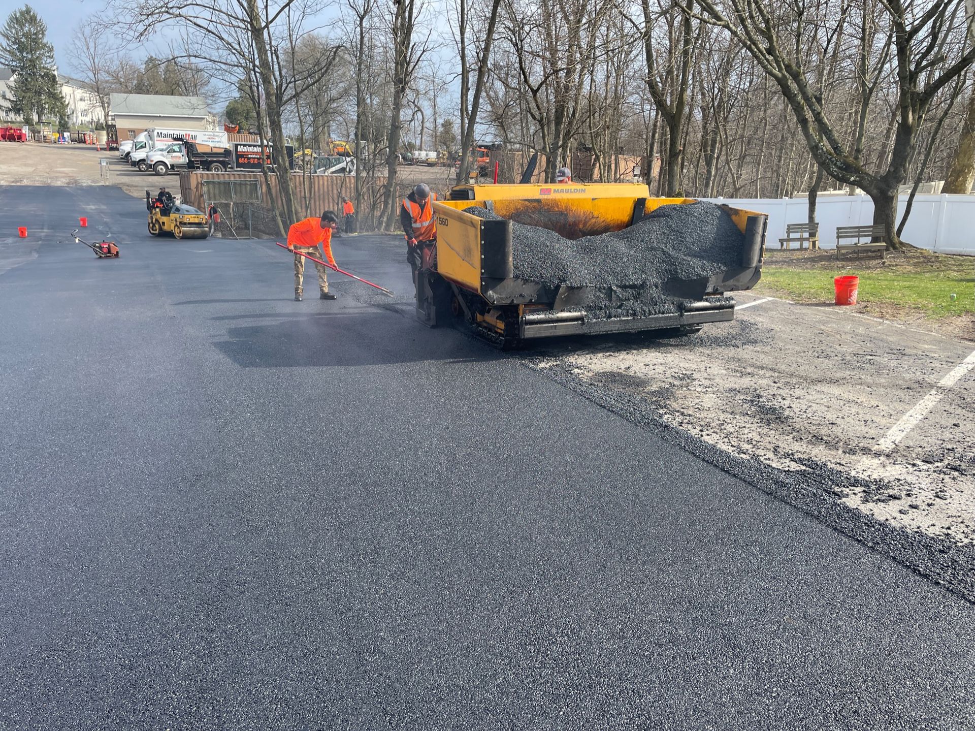 Construction crew uses an asphalt paving machine to lay fresh blacktop in an outdoor parking area.