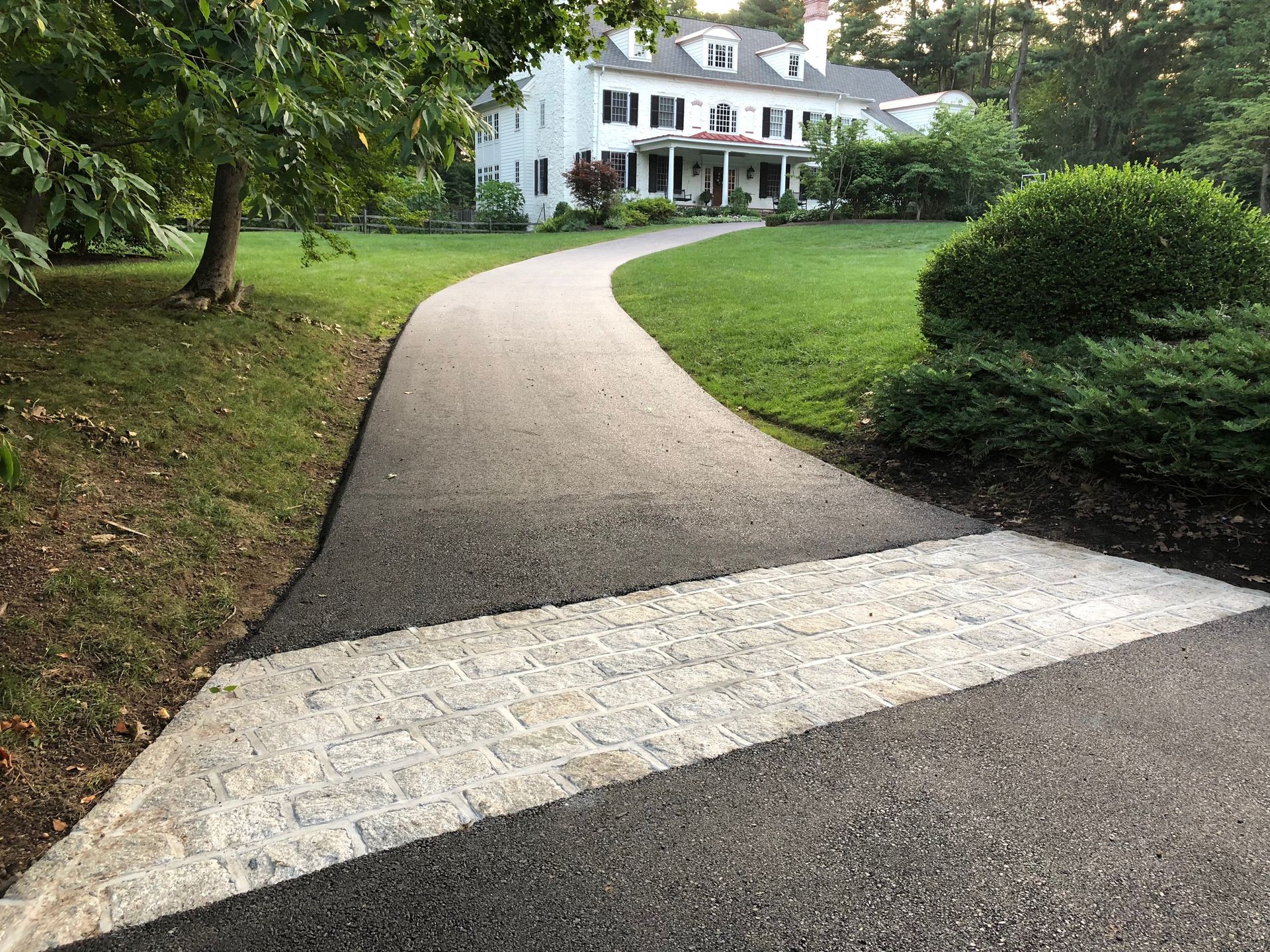 A white house at the end of a paved driveway featuring a decorative stone crosswalk transition.
