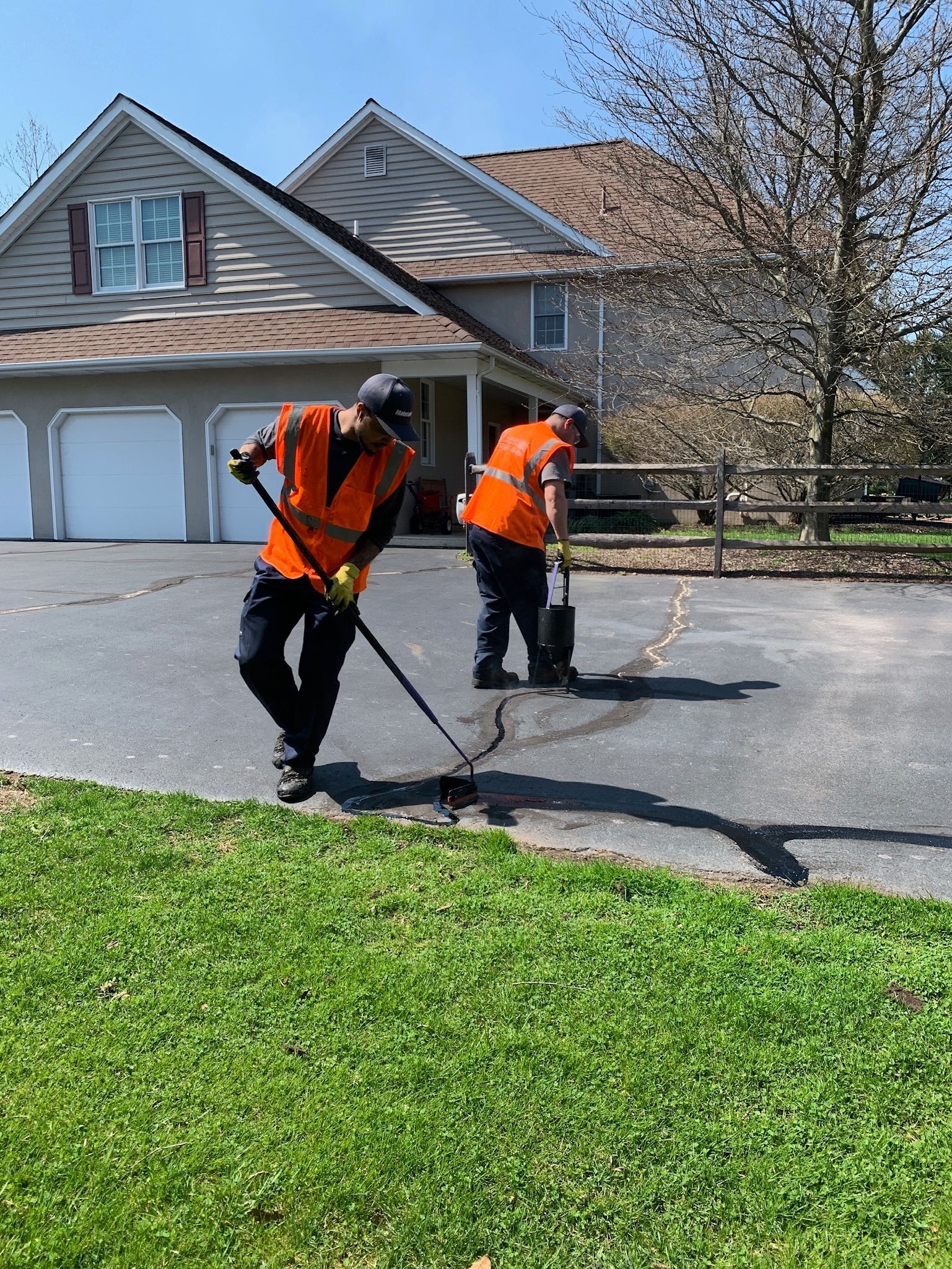 Two workers in orange safety vests repair cracks in a residential driveway with tools.