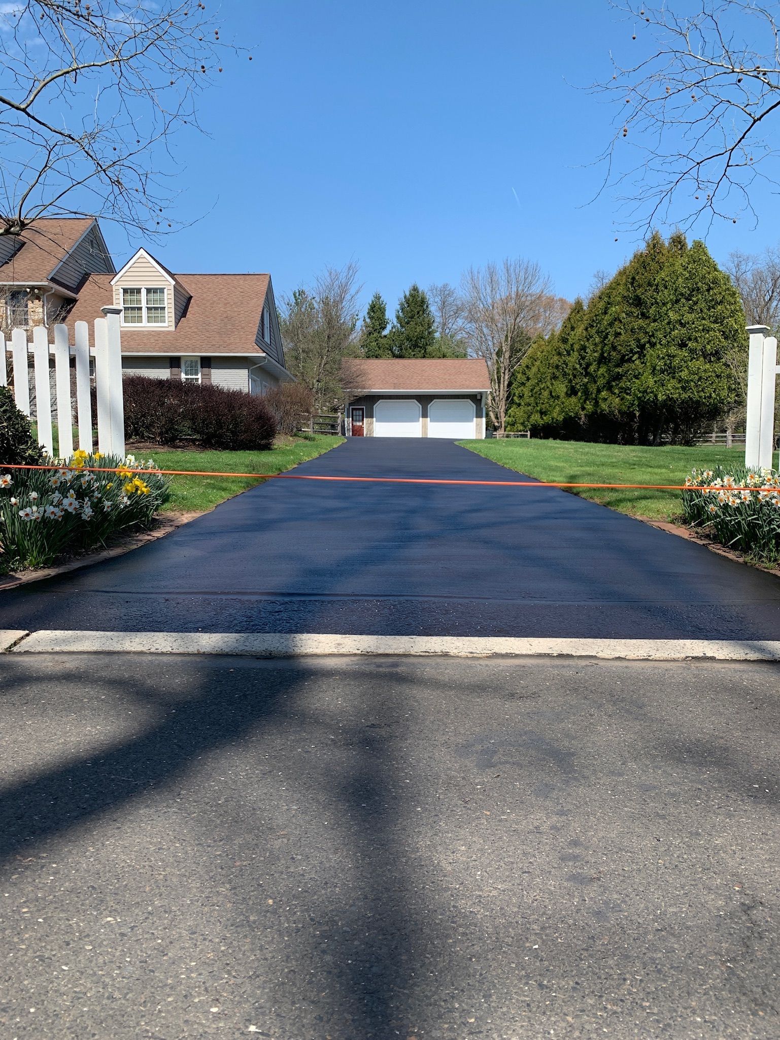A freshly paved, dark asphalt driveway leads to a detached two-car garage between two residential properties.