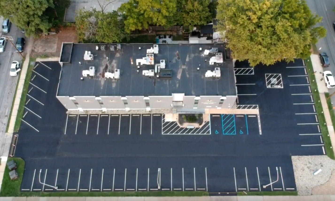 An aerial view of a freshly paved commercial parking lot surrounding a rectangular office building with a flat roof.