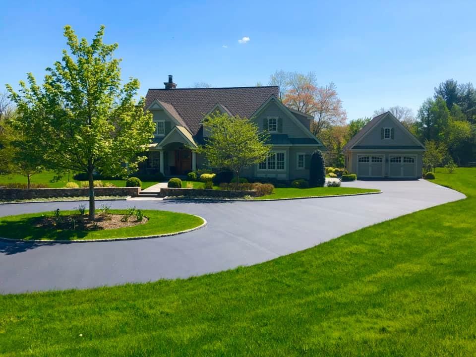 A multi-story house with a detached garage and a large, paved circular driveway surrounded by a green lawn and trees.