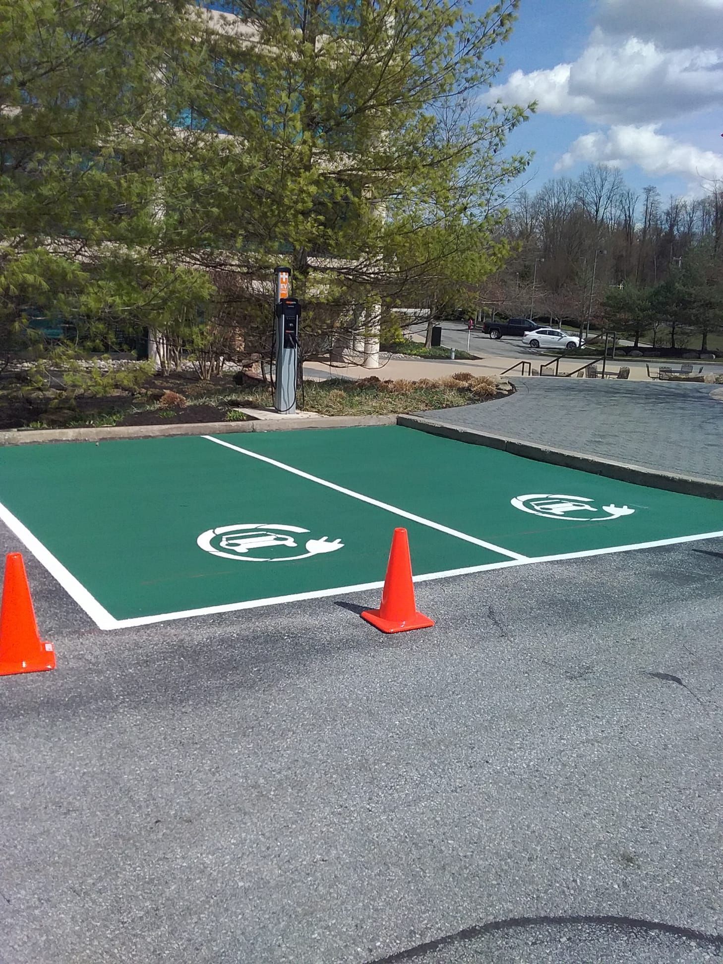 Two electric vehicle parking spaces painted green with white EV symbols and boundary lines, marked by two orange traffic cones.