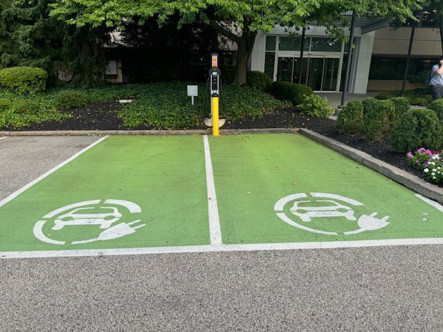 Two green-painted electric vehicle charging parking spaces with white car and plug icons, featuring a central charger post.