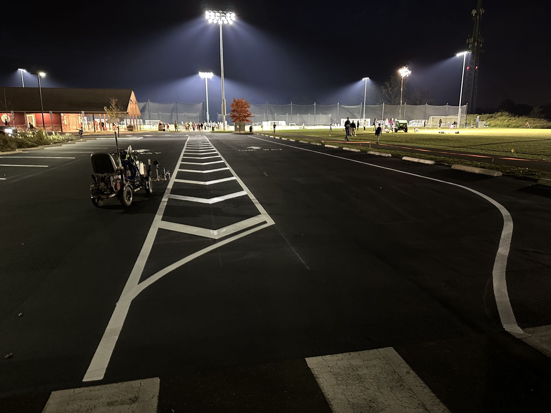 An empty, freshly painted  parking lot at night, illuminated by bright stadium lights over a nearby field.