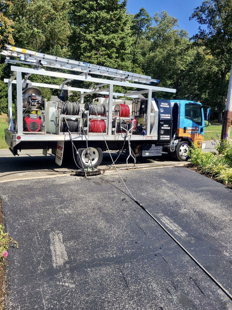 A white pickup truck towing equipment and a blue and orange utility truck parked on a residential street.