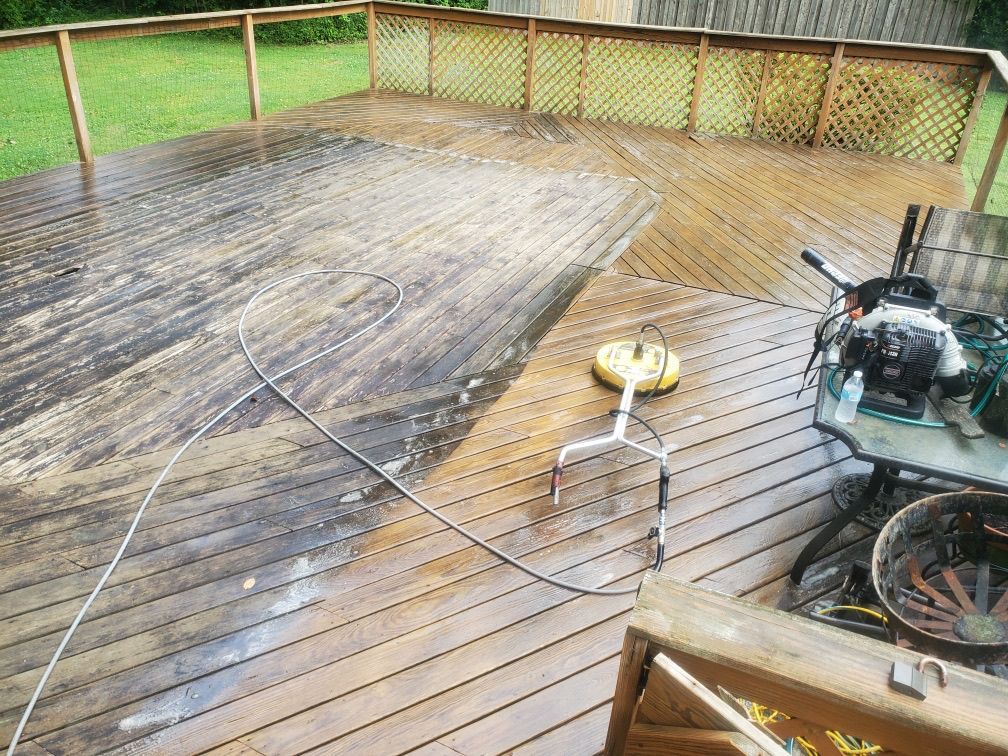A partially pressure-washed wooden deck with a surface cleaner tool sitting on the cleaned section.