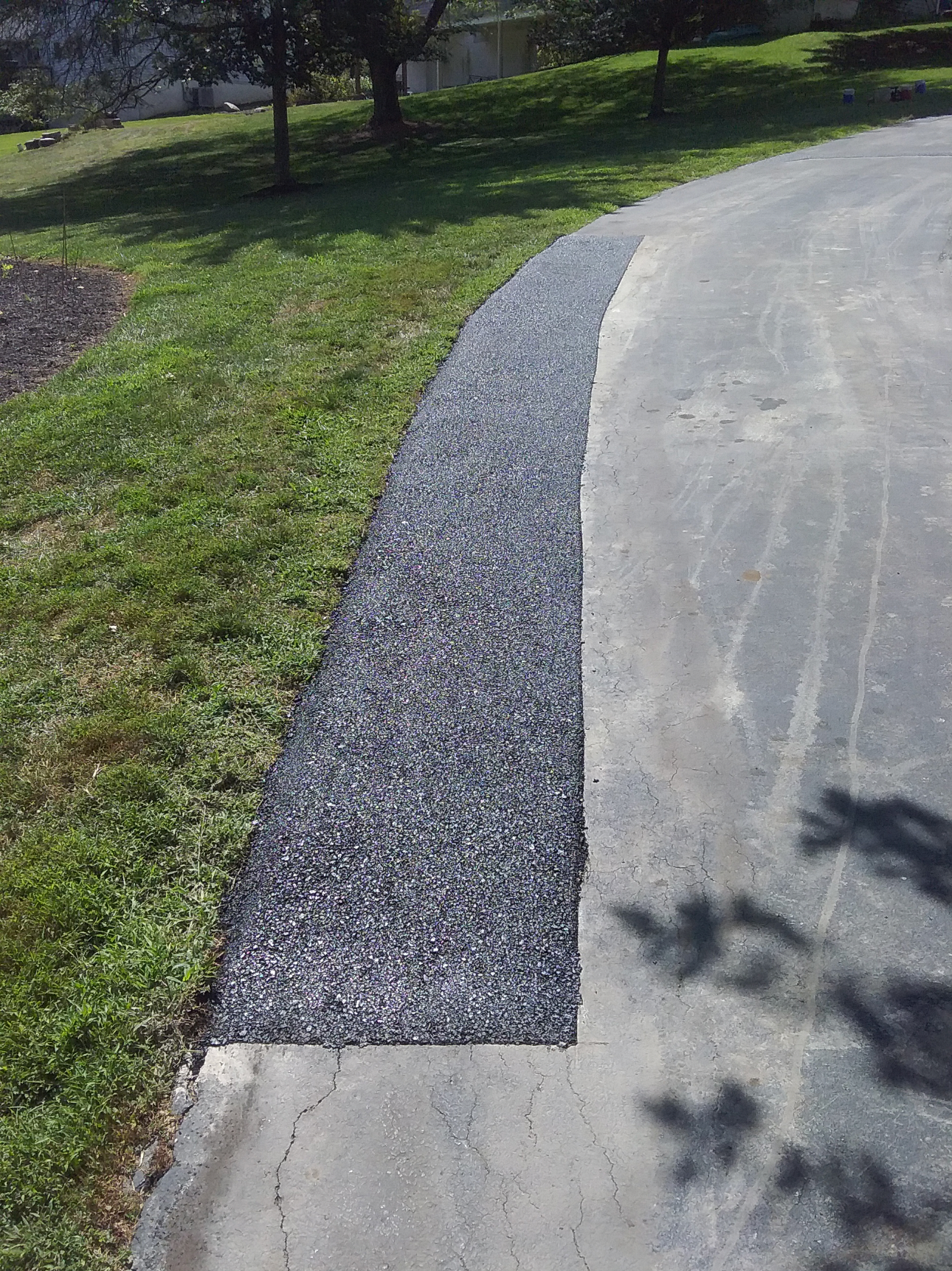 An asphalt driveway with a distinct color contrast, showing a smooth, darker sealed section next to a coarser, lighter strip.