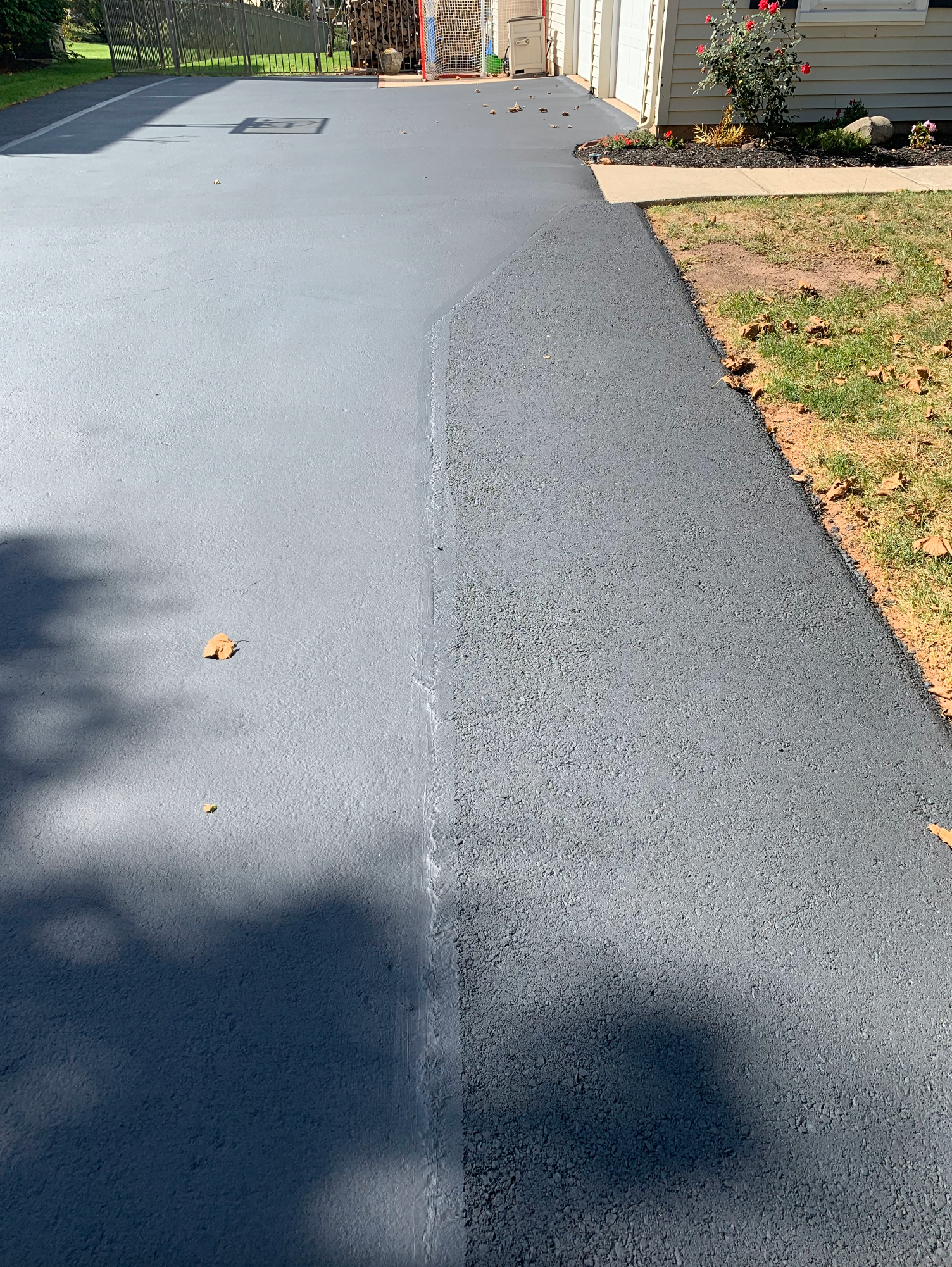 A view of a driveway showing a sharp contrast between a smooth, light grey sealed section and a dark, rough patch.
