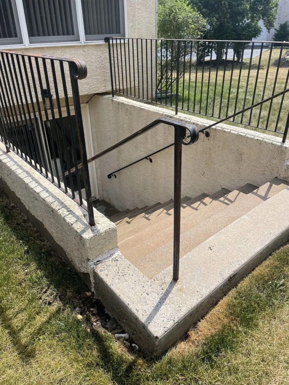 Concrete staircase leading down to a basement entrance with black metal handrails and a matching fence.