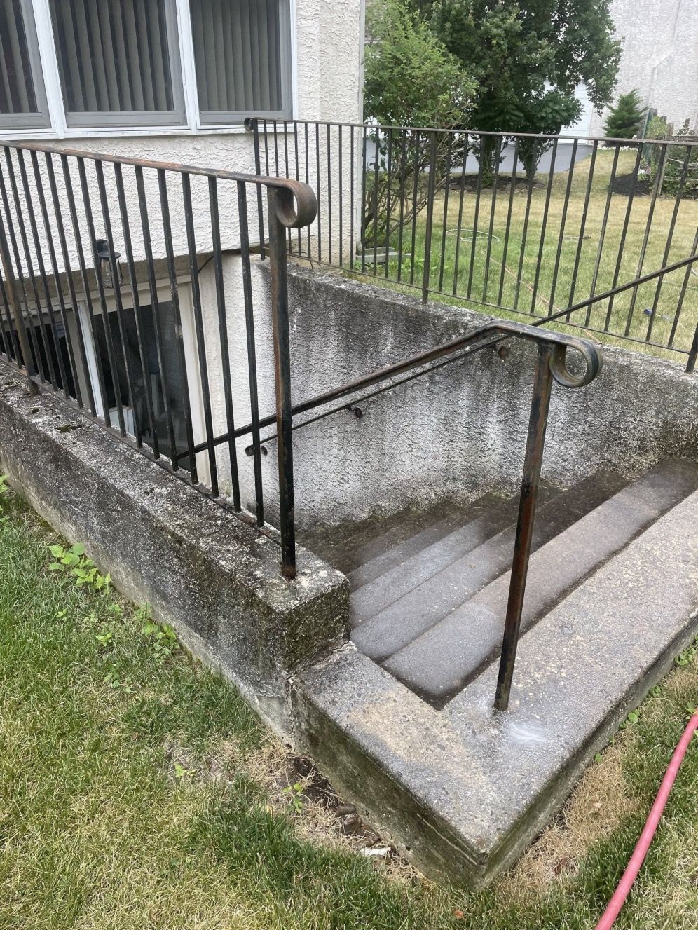 Concrete basement entrance with metal railing and steps leading down. Green grass surrounds.