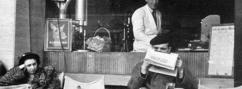 A cafe scene with a person reading a newspaper, a woman sitting nearby, and a worker behind the counter.