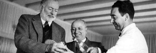 Ernest Hemingway (left) and two other men in suits share a drink and smile in an indoor setting.