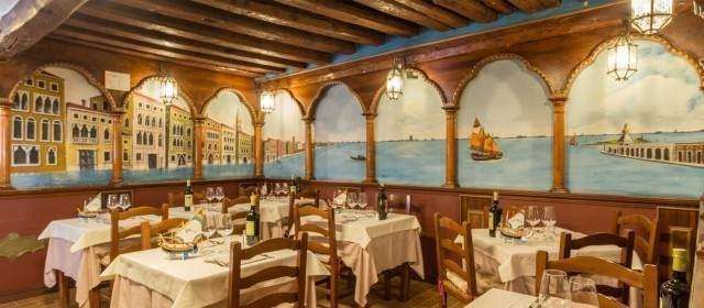 A rustic restaurant dining room with multiple white-clothed tables and a wall mural depicting a Venetian cityscape.